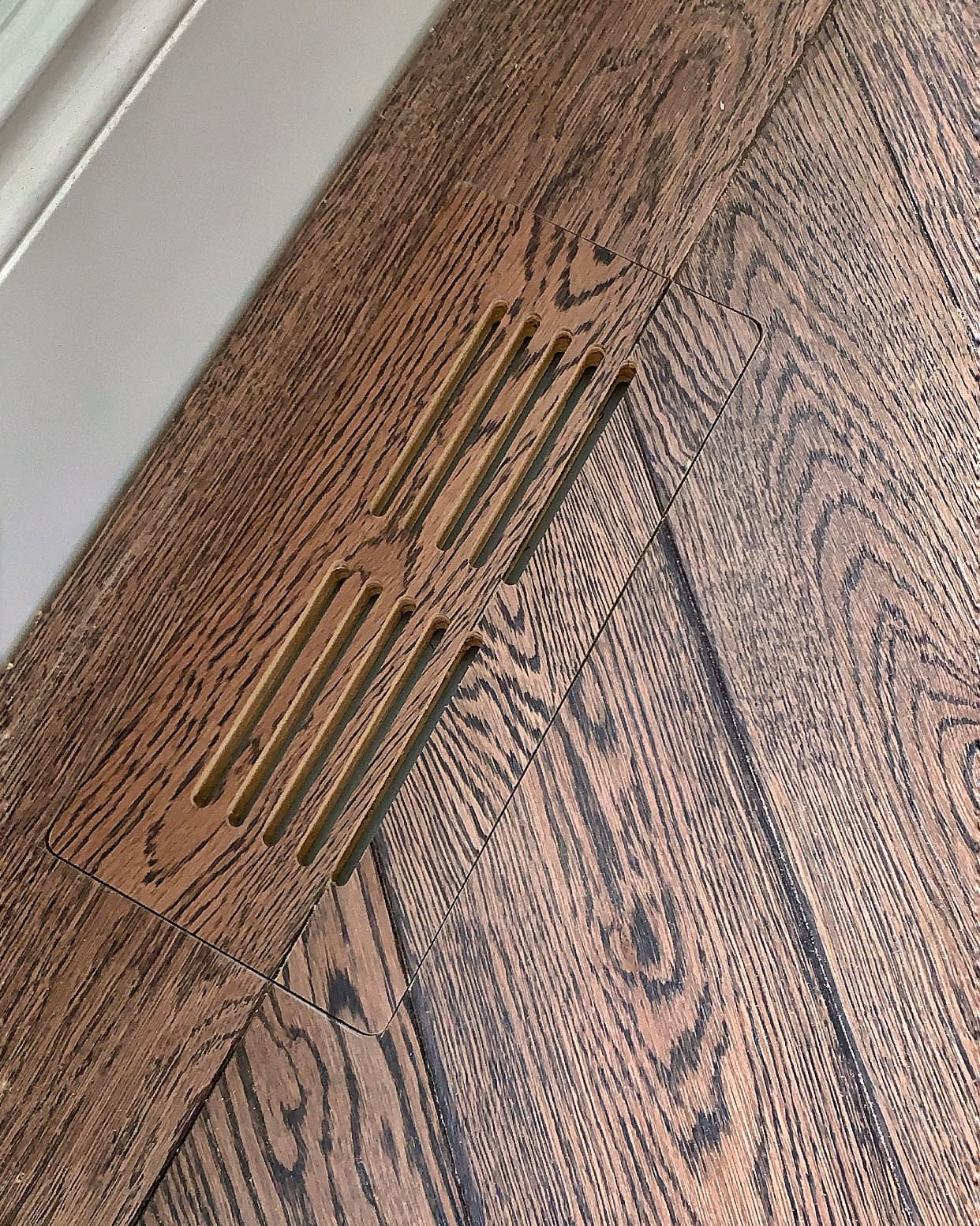Close detail of a custom floor vent cut into dark hardwood with matched grain direction