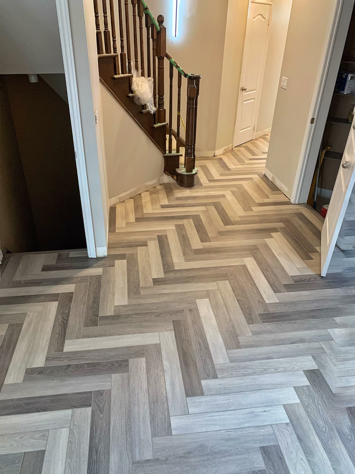 Herringbone-pattern luxury vinyl flooring in an entryway beside a staircase