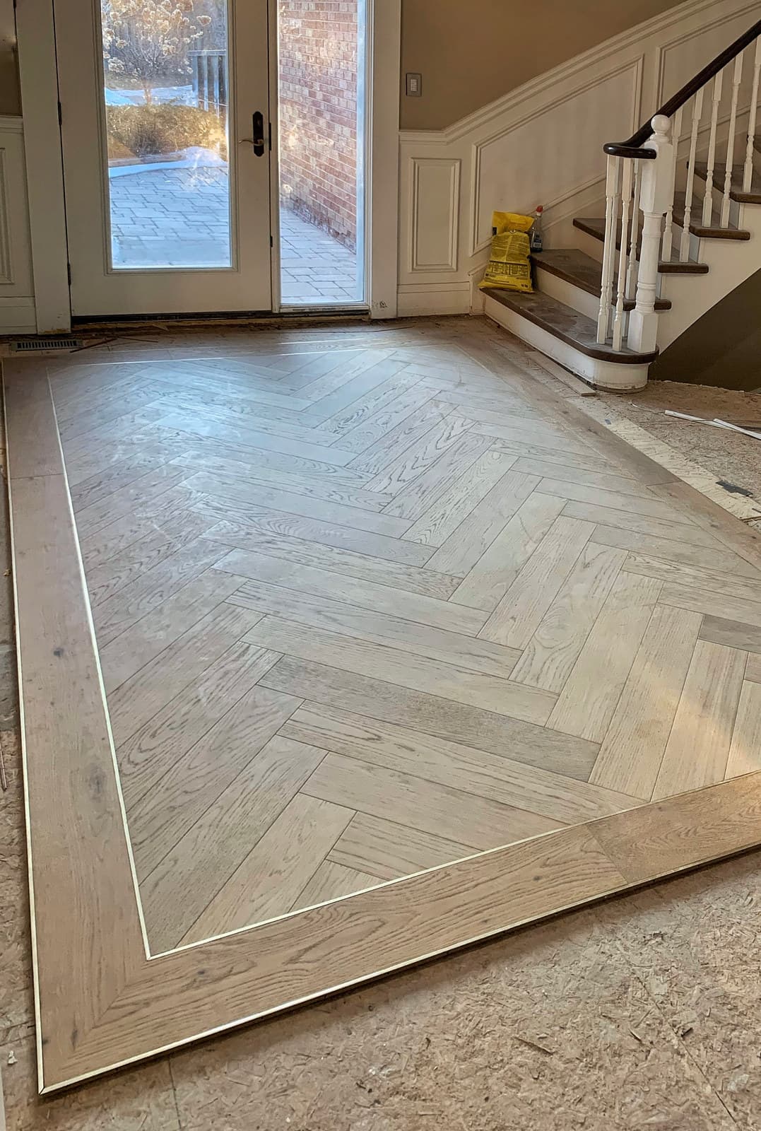 A picture-framed herringbone floor meeting a curved bottom stair
