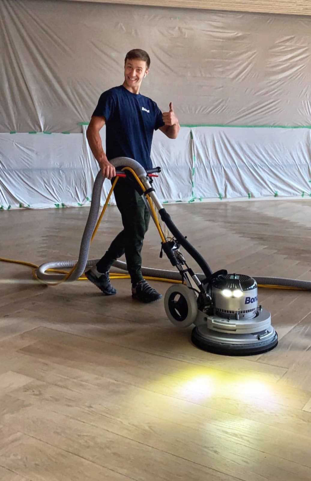 A Woodstellar team member sanding a hardwood floor beneath protective dust sheeting