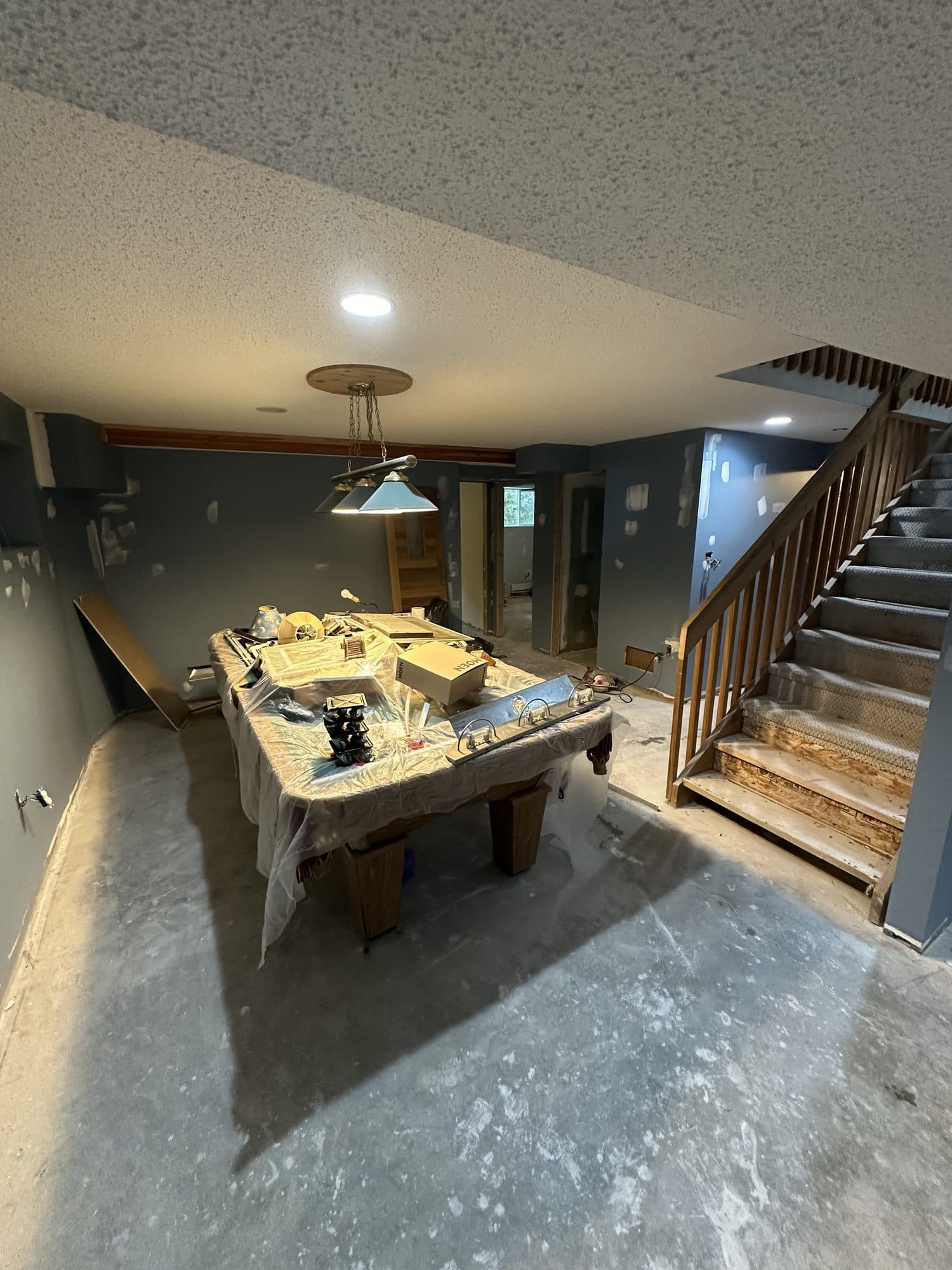 A basement games room with a bare concrete floor and raw stair before renovation