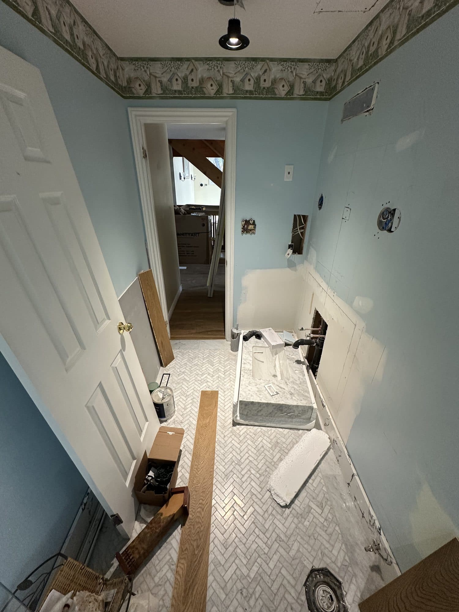 A narrow bathroom with blue walls and a herringbone marble floor before renovation