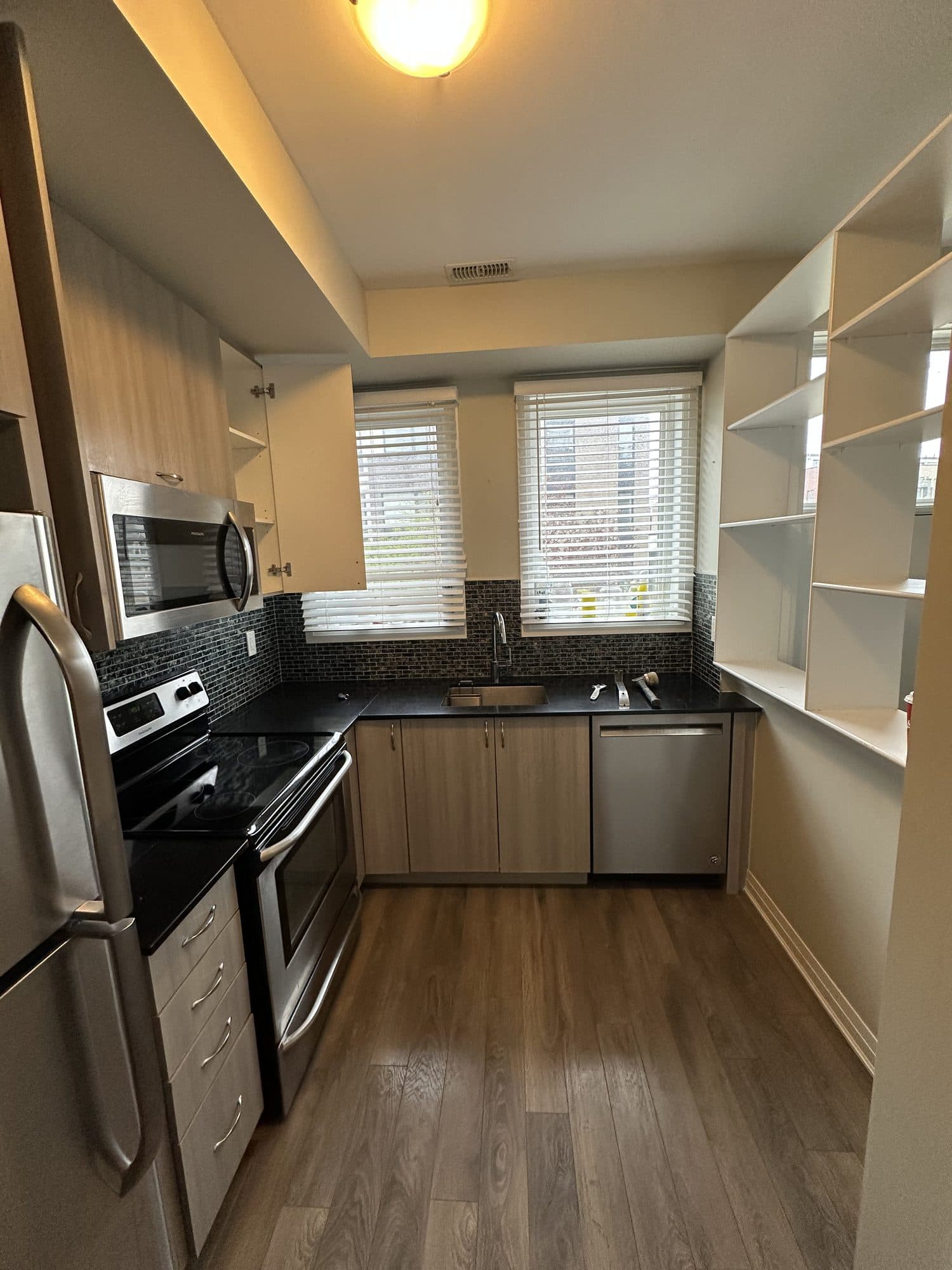 A tired kitchen with dark backsplash and open shelving before renovation