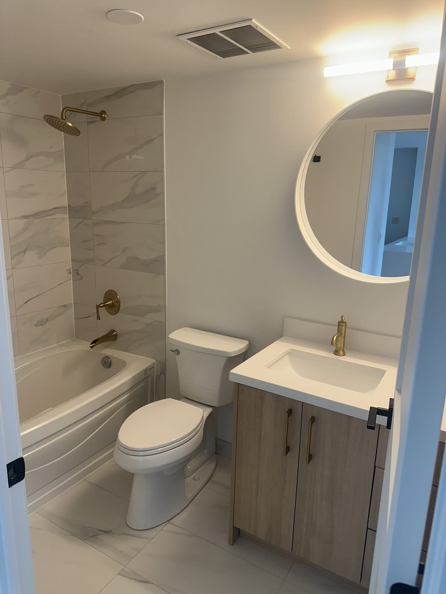 The same bathroom rebuilt with marble tile, a floating vanity and round mirror