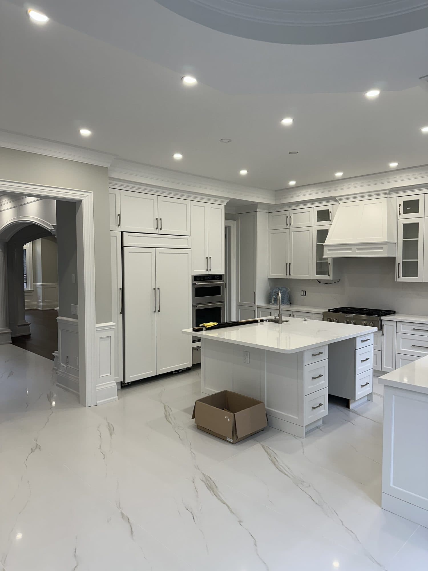 A white custom kitchen with a quartz island and marble floor beneath a domed ceiling