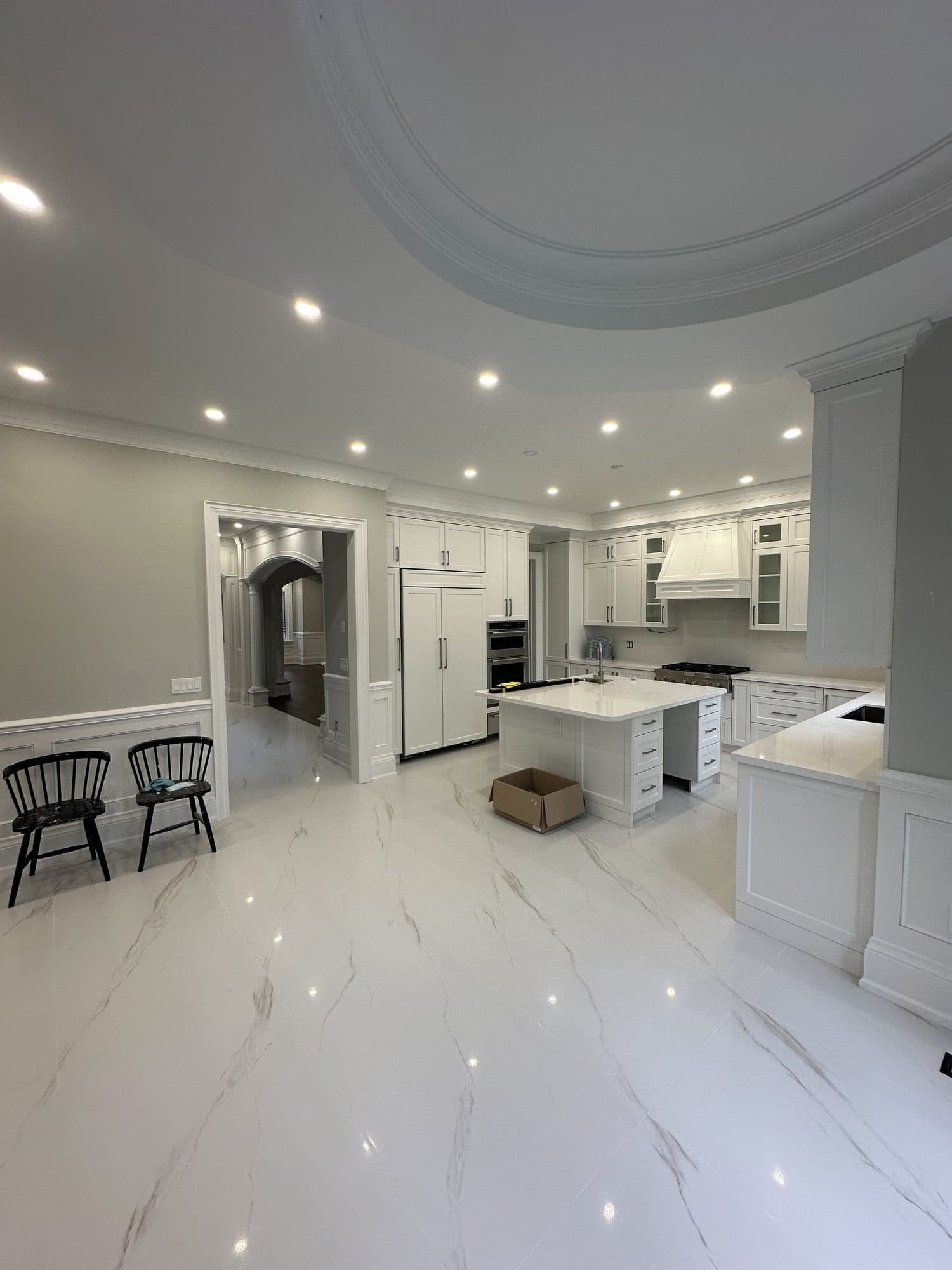 An open white kitchen with a quartz island and polished marble floor