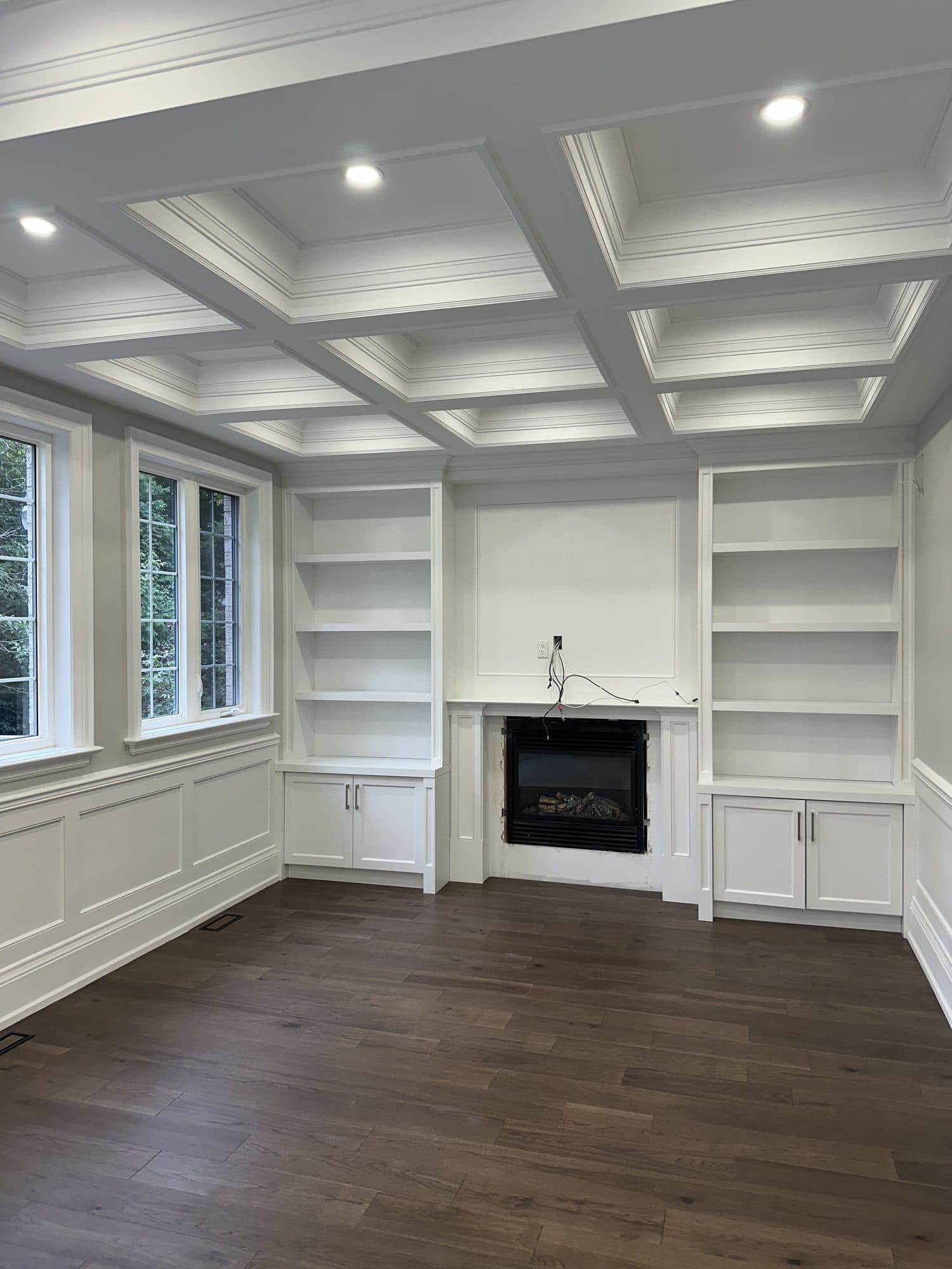 A panelled study with a coffered ceiling, white built-in shelving and a dark hardwood floor