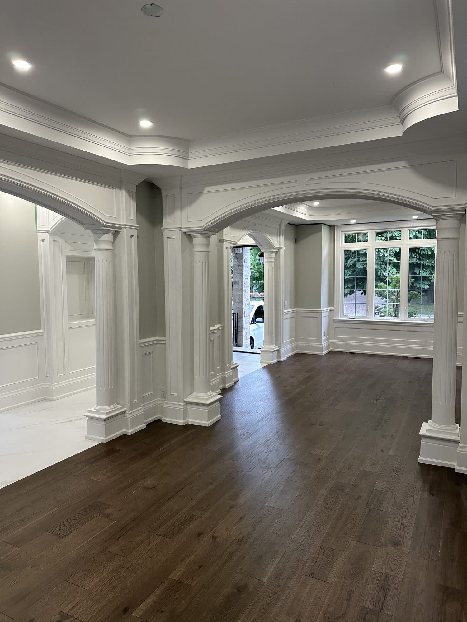 An open living space with fluted columns, arched openings and a dark hardwood floor
