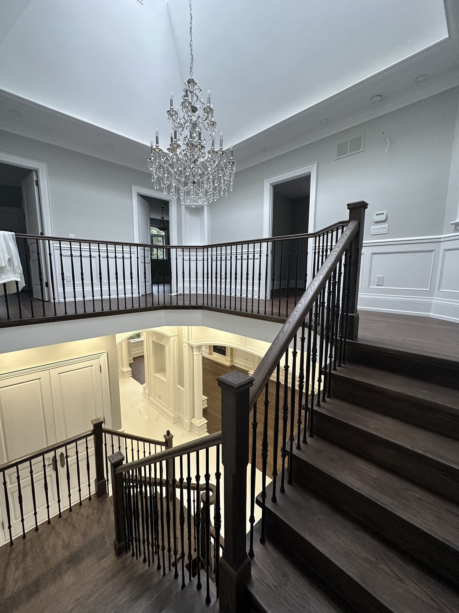 A staircase landing beneath a crystal chandelier, with dark oak treads and iron balusters