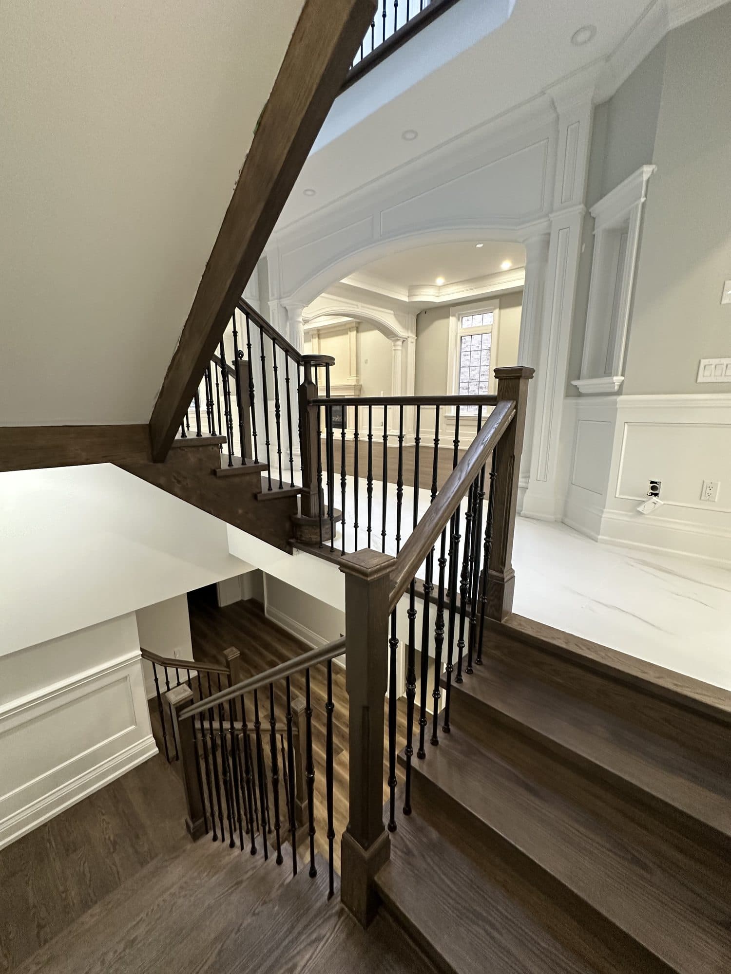A finished oak staircase with dark treads and iron balusters over marble and hardwood