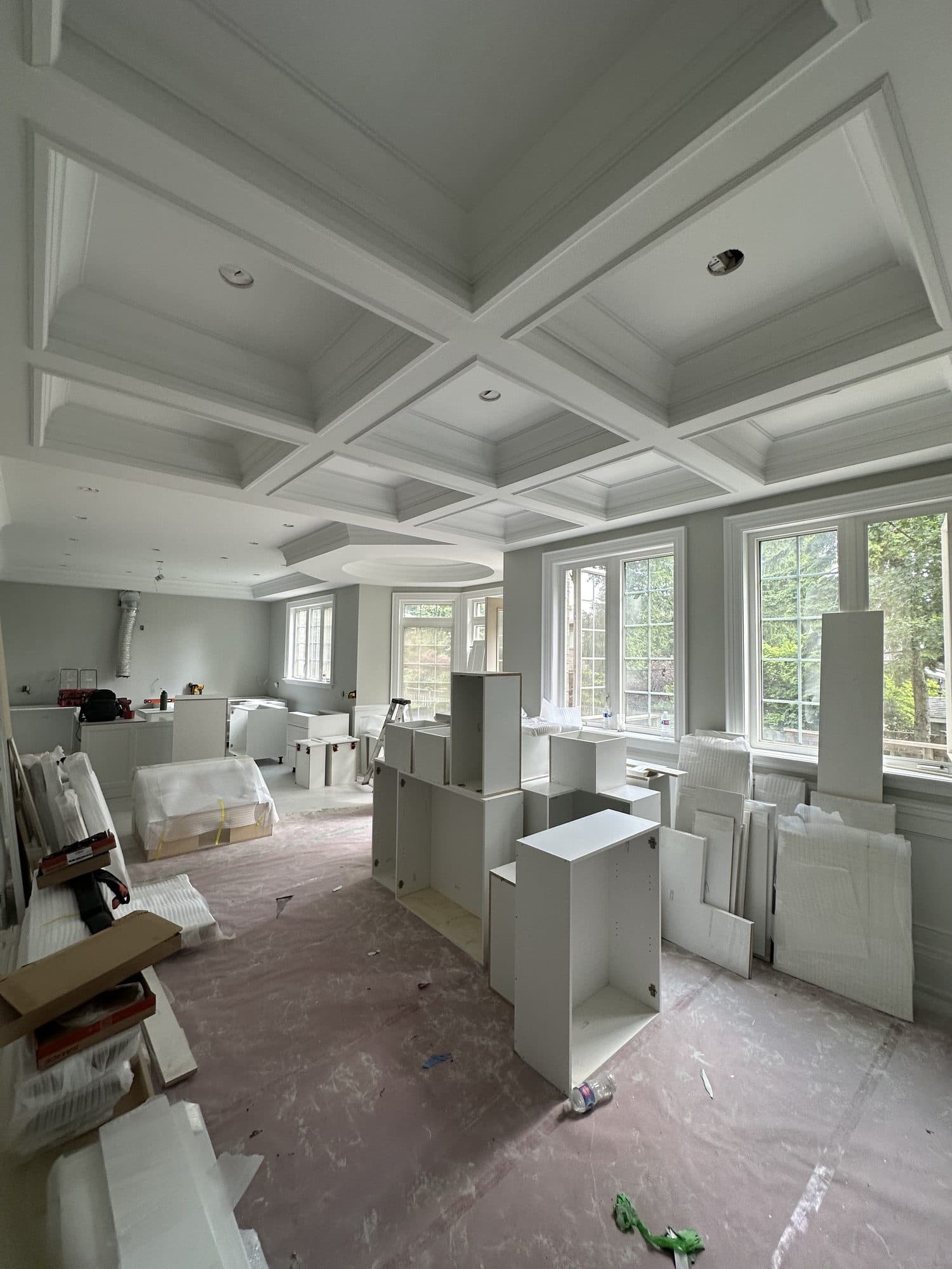 A kitchen with a finished coffered ceiling as the cabinetry is installed
