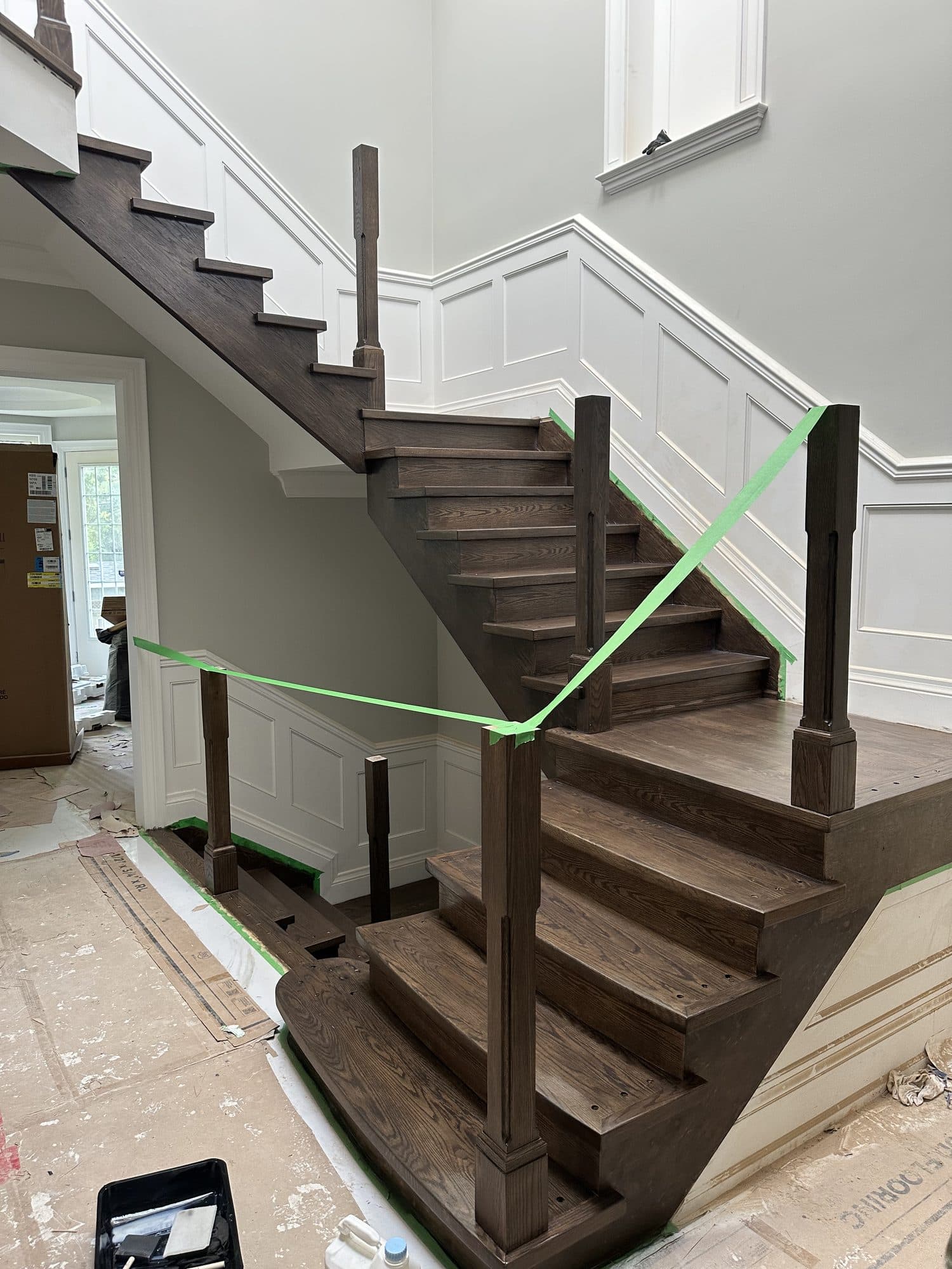 A completed dark-stained oak staircase with wainscoting and iron balusters