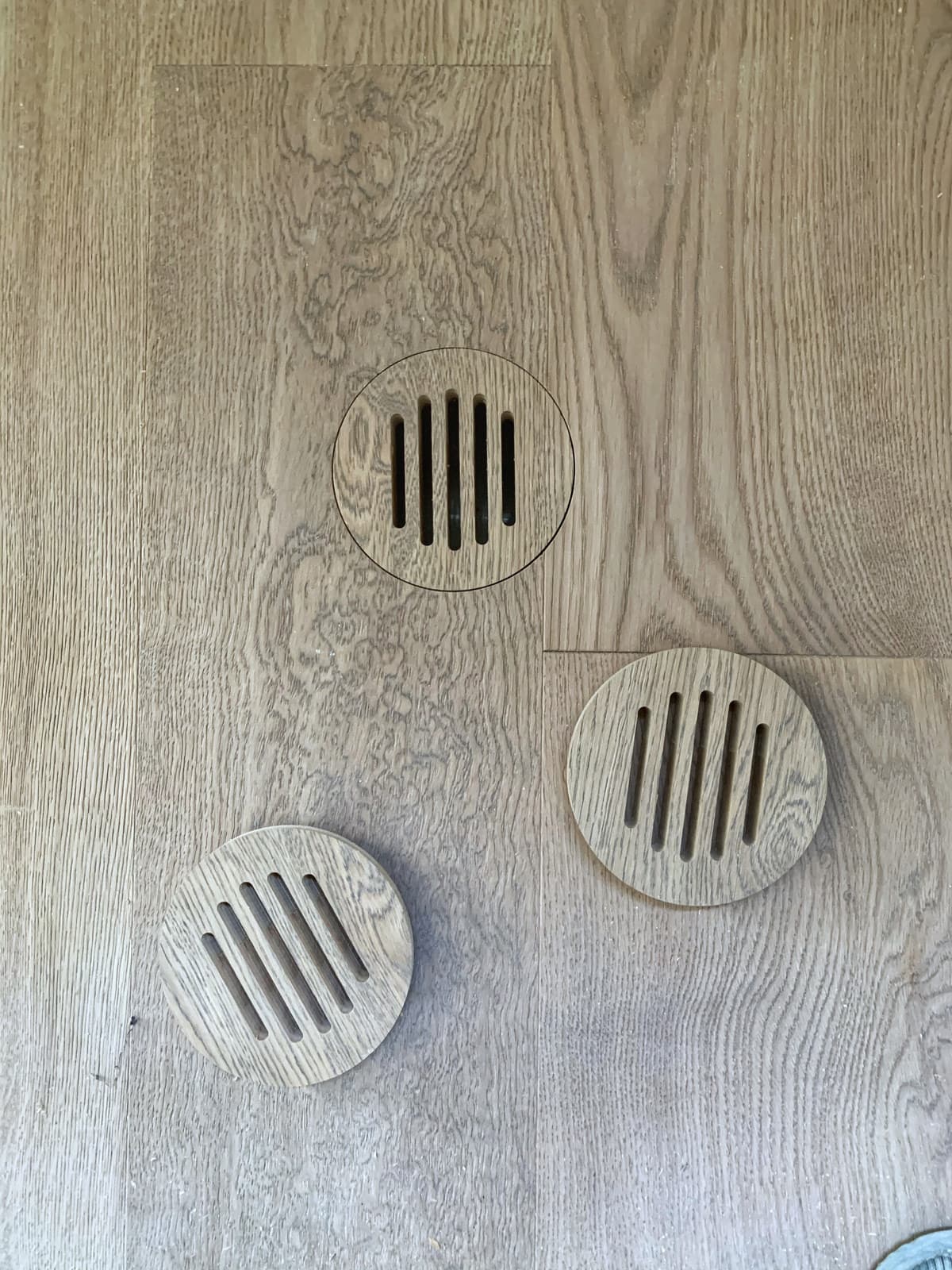A pair of round custom floor vents fitted into an oak floor with matched grain
