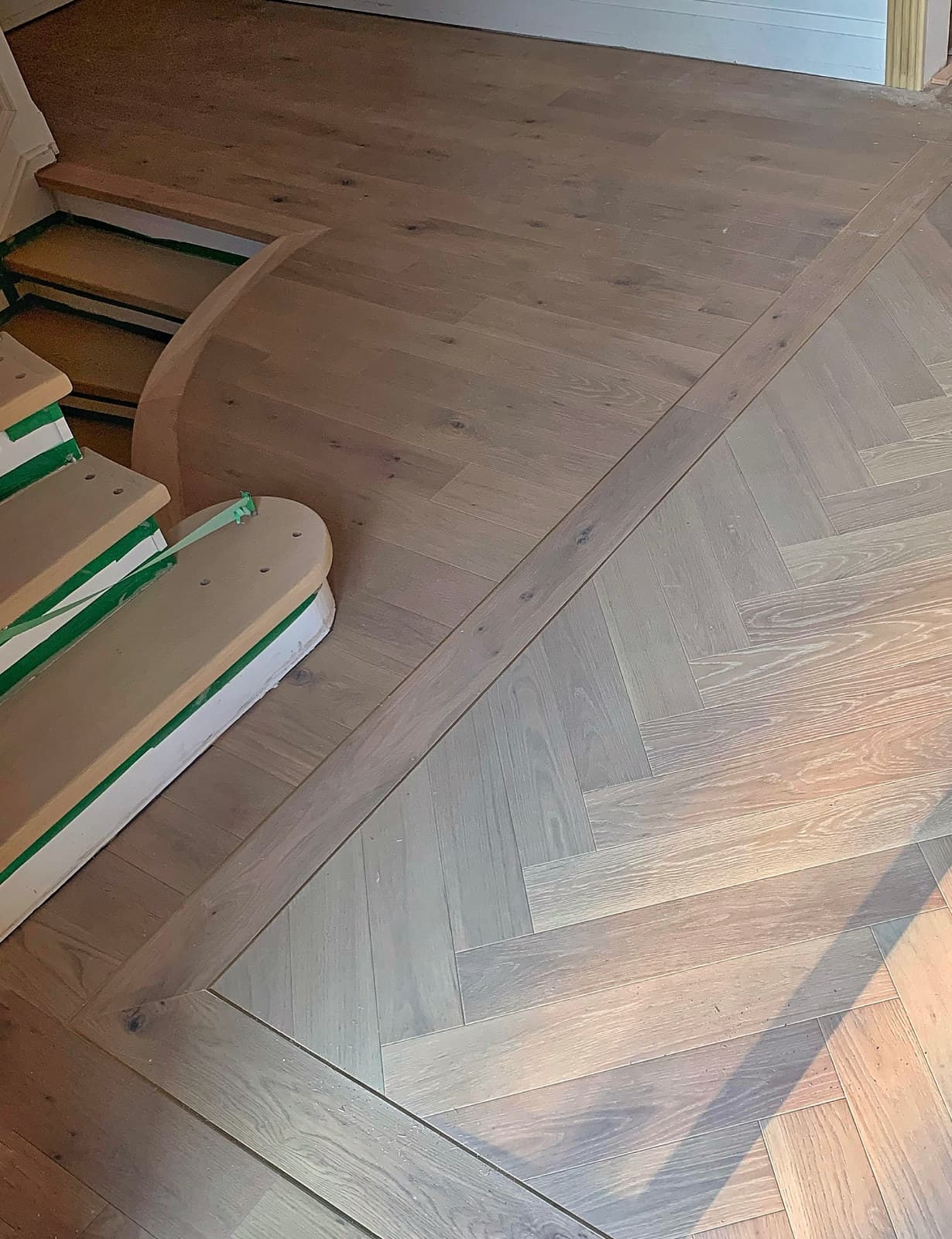 Herringbone hardwood meeting the curved base of a staircase