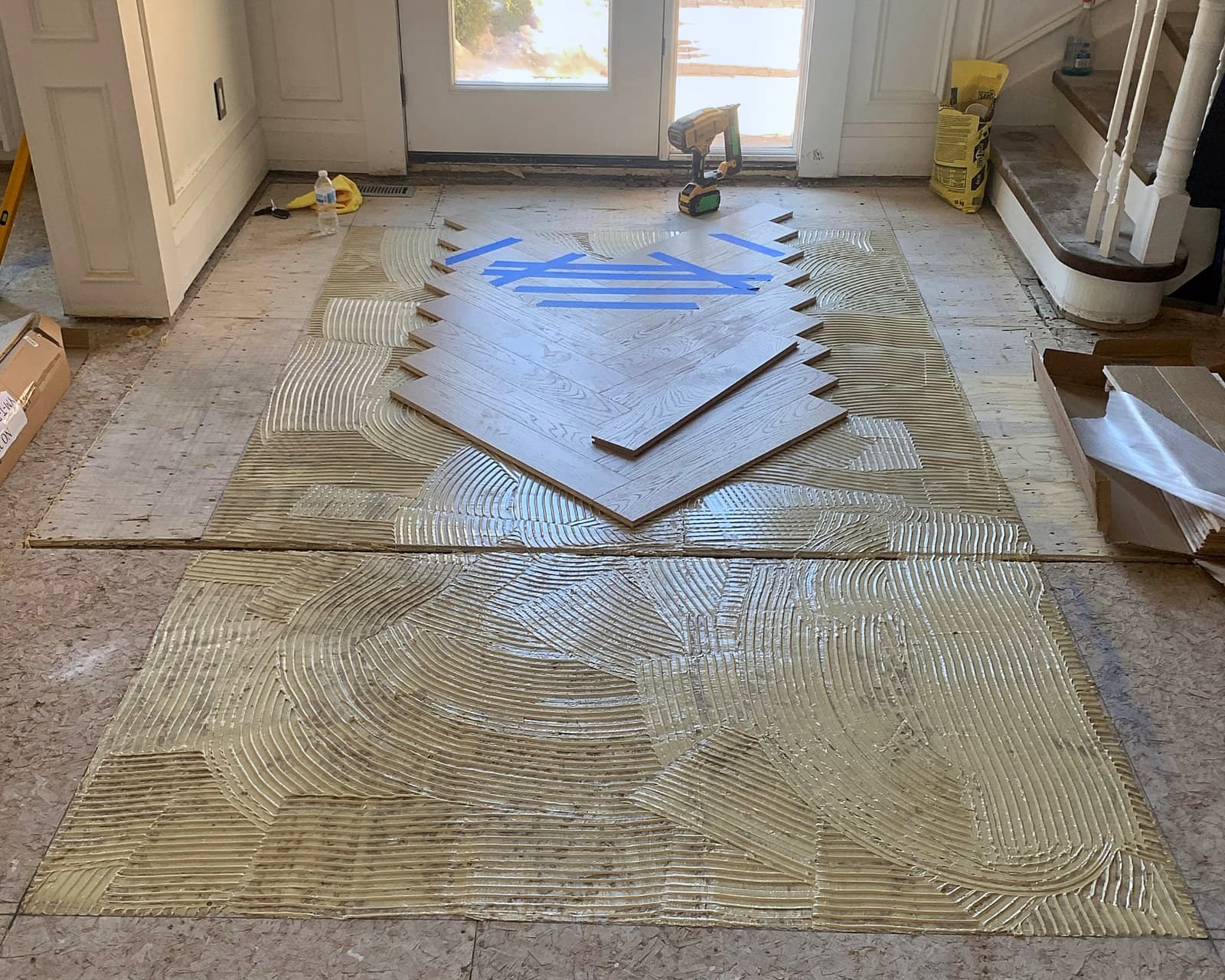 Herringbone hardwood being set into troweled adhesive at a home entry