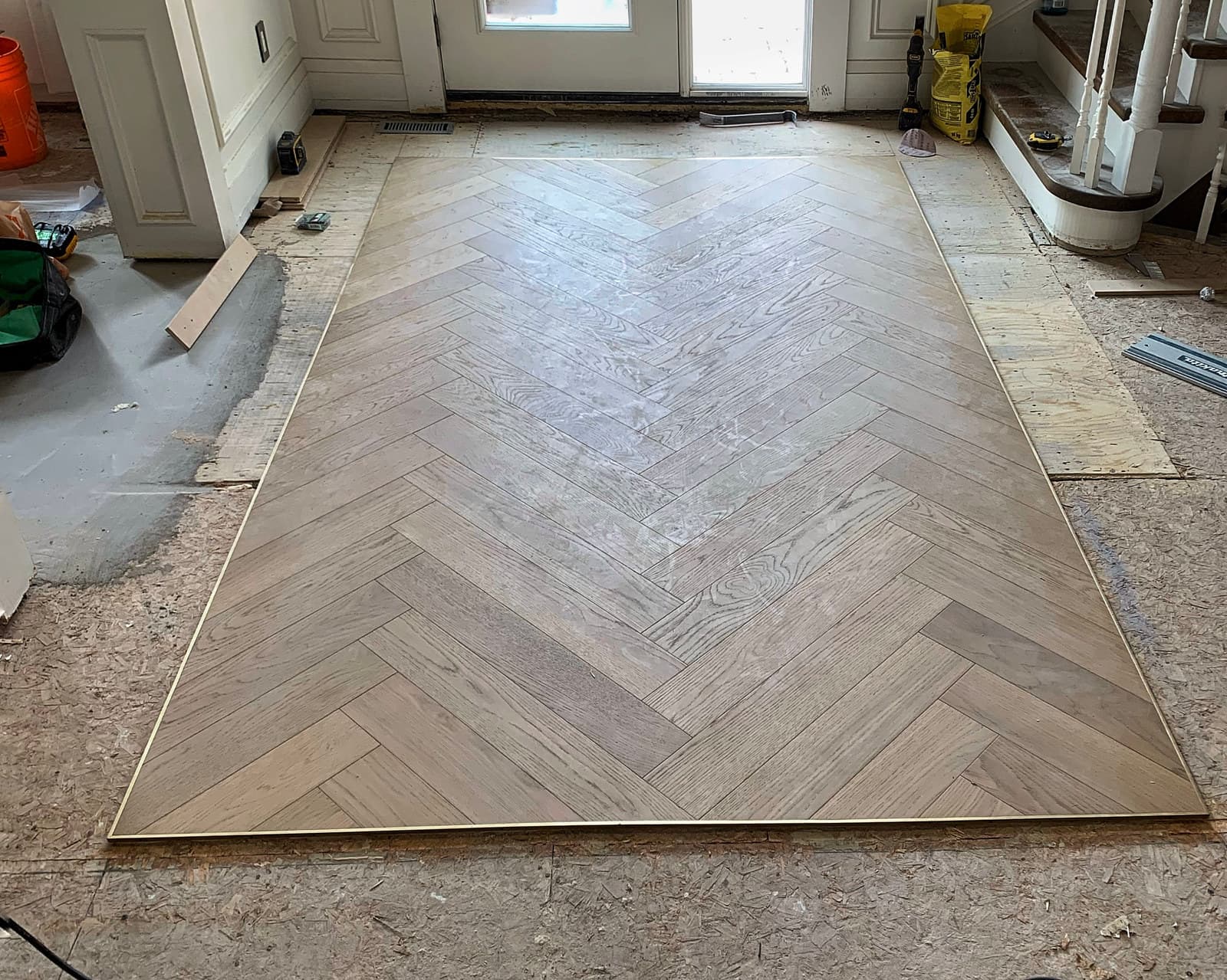 A herringbone hardwood floor nearing completion across an open room