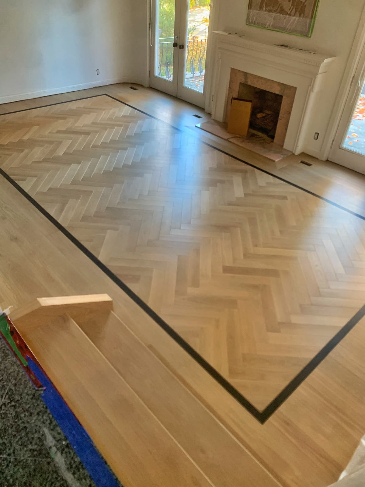 A picture-framed herringbone hardwood floor in a room with a fireplace