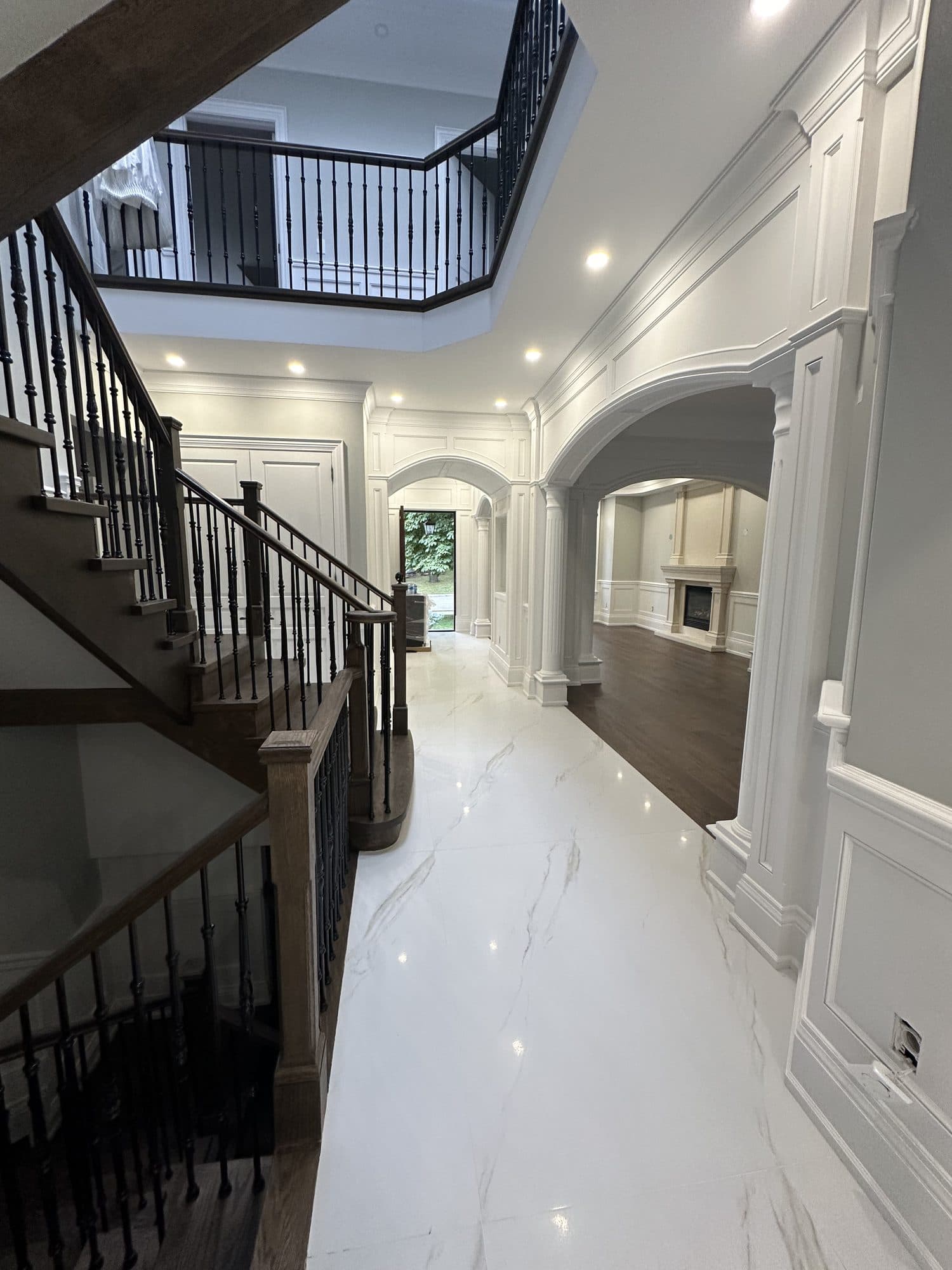 A grand two-storey foyer with a curved oak staircase, iron balusters and a marble floor